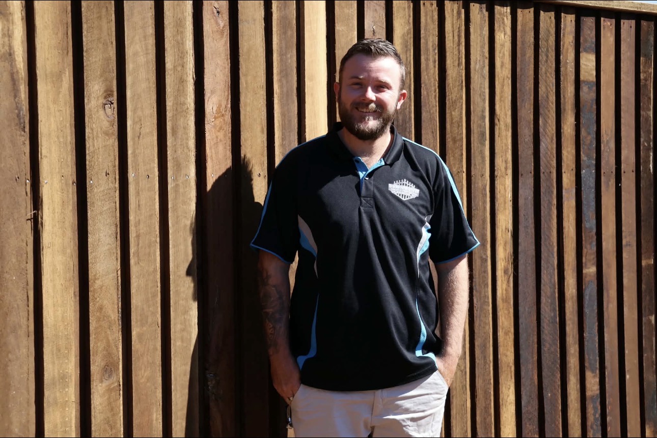 Caleb, owner-operator of Iron Clad Fencing & Construction, standing in front of a hardwood timber fence